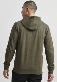 Olivengrønn hettegenser i mykt teksturert stoff, med avslappet passform, ribbestrikkede mansjetter og kant, med et enkelt, minimalistisk design.