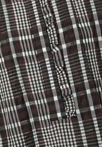 Tecido quadriculado em preto e branco apresentando vários padrões de xadrez, com uma borda franzida que destaca a textura e os detalhes do design.