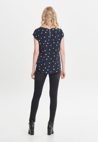 Kortærmet marineblå bluse med guldprikker, detalje med nøglehul bagpå, parret med sorte skinny jeans og ankelstøvler.