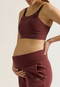 Soutien-gorge de maternité en bordeaux, fabriqué en tissu côtelé. Il dispose de bretelles réglables et d'un logo. Pantalon taille haute assorti dans une couleur similaire.