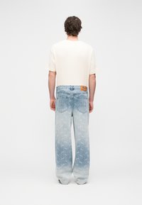 Lichtgekleurd geribd T-shirt en vervaagde blauwe spijkerbroek met een gradiëntpatroon en geborduurde details op de achterzakken.