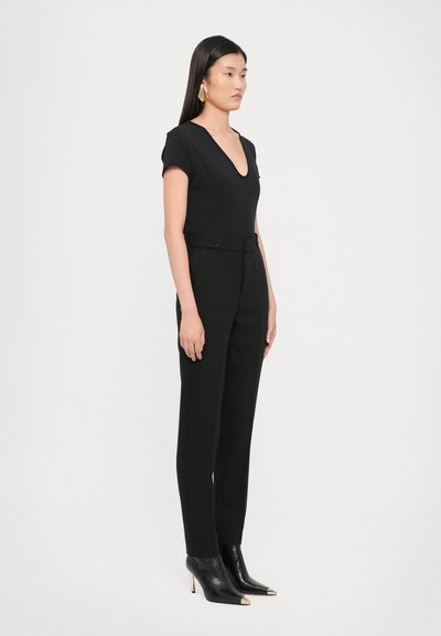 Top nero aderente con scollatura profonda a V, abbinato a pantaloni neri a vita alta con chiusura a bottone e eleganti stivali neri con tacco alto.