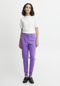 Vit crew neck t-shirt i kombination med lila skinny-byxor. Byxorna har framfickor och en slät textur. Svarta slip-on skor.