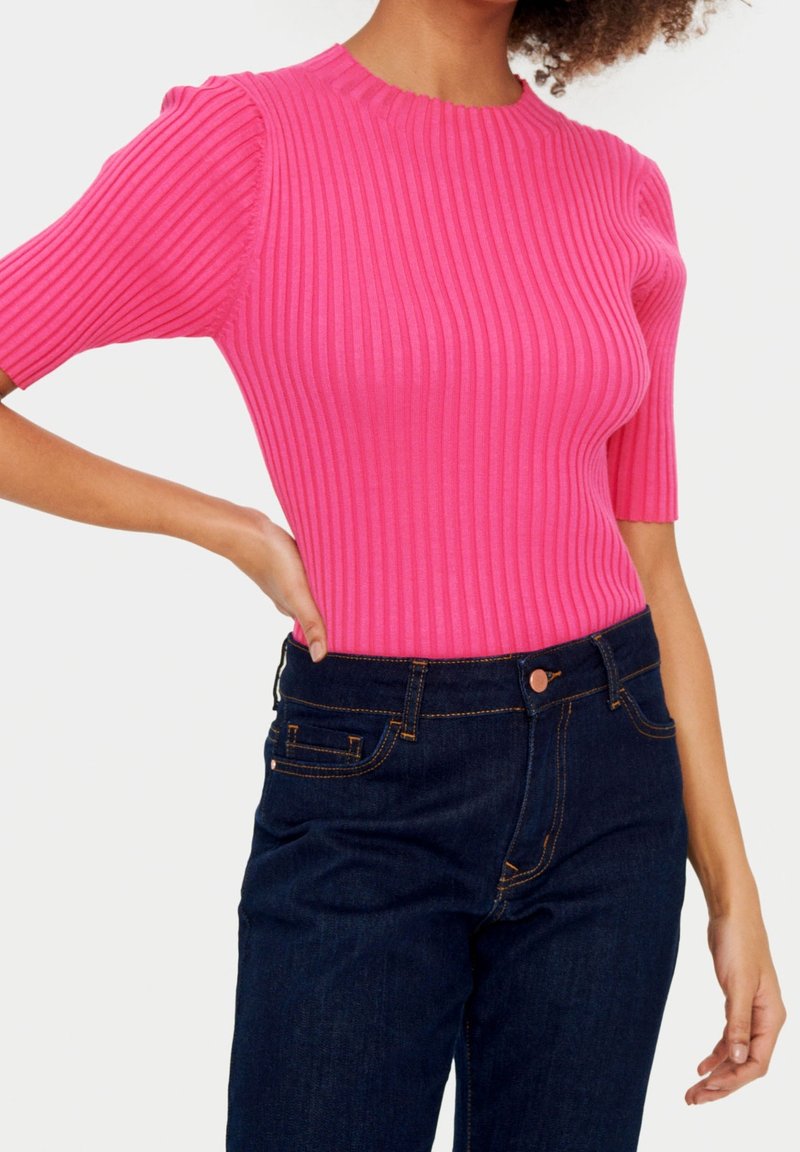 Haut rose à manches courtes côtelé avec un col rond, associé à un jean taille haute bleu foncé avec des coutures oranges et des poches classiques.