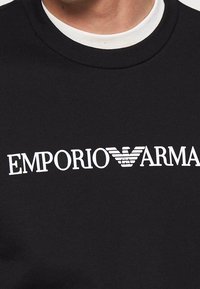 Felpa nera con logo bianco "EMPORIO ARMANI" e aquila stilizzata. Collo rotondo e texture in cotone morbido.