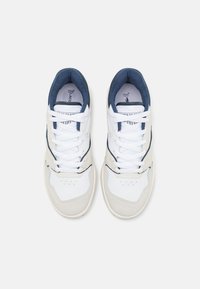 Zapatillas blancas con acentos en navy, con un diseño de cuero suave, puntera de gamuza y cordones planos pasados por seis ojales.