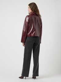 Burgundy leather jacket with a glossy finish, featuring a simple collar and zip closure, paired with high-waisted dark gray pants.