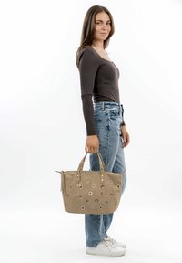 Bolso beige hecho de ante, con recortes circulares y ojales plateados. Dos asas cortas y una correa desmontable para mayor versatilidad.