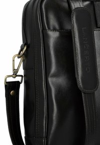 Czarna skórzana torba o gładkiej fakturze, wyraźnym przeszyciu, regulowanym pasku z metalowymi akcentami oraz wytłoczonym logo z boku.