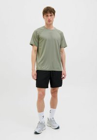 Športový outfit, ktorý sa skladá zo svetlozeleného trička s krátkym rukávom a čiernych šortiek, so šedými športovými topánkami a bielymi ponožkami. Jednoduchý, funkčný dizajn.