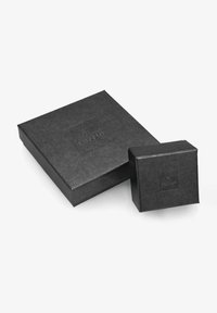 Due scatole nere in carta strutturata, una grande e rettangolare, l'altra piccola e quadrata, entrambe con un logo in rilievo sulla superficie.