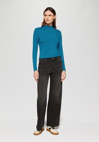 Langsleeve teal top met een hoge hals, gecombineerd met brede zwarte jeans en beige sneakers met zwarte veters. Eenvoudig ontwerp, effen kleuren.