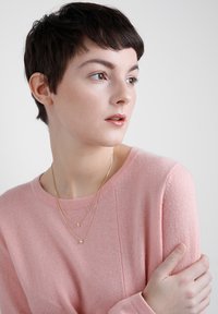 Lyserød sweater lavet af blødt stof, med rund halsudskæring og lange ærmer, parret med delikate gyldne lagkæder.