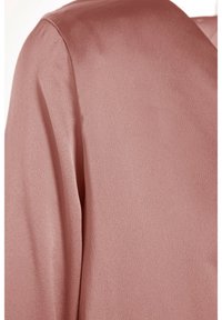 Gros plan d'un tissu rose poussiéreux doux et texturé montrant l'épaule et la partie supérieure de la manche d'un vêtement.