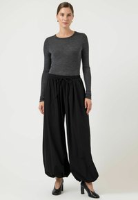 Czarne spodnie o szerokich nogawkach z elastycznym paskiem i sznurkiem, zestawione z dopasowaną szarą koszulką z długim rękawem oraz czarnymi butami na obcasie.
