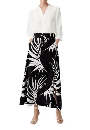 White blouse with roll-up sleeves and a black skirt featuring a white palm leaf print. Skirt has a high slit and side pockets.