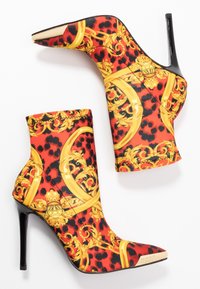 Stivaletti con tacco alto in tessuto stampato leopardato rosso e nero, con motivi dorati ornamentali e punta affusolata. Tacco a spillo nero.