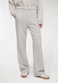 Szare dresy wykonane z miękkiego materiału, charakteryzujące się luźnym krojem, szerokimi nogawkami oraz elastycznym pasem z bocznymi kieszeniami.