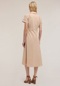 Knee-length beige dress with short sleeves, collared design, and open stitch accents on shoulders, paired with brown strappy heel sandals.
