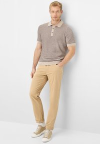 Beige gebreid poloshirt met korte mouwen en drieknopenlijst, gecombineerd met lichtbruine chino's en beige sneakers, met witte sokken.