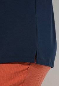 Camisa de manga corta azul marino con aberturas laterales, combinada con pantalones texturizados de color óxido. Ambos artículos presentan líneas simples y limpias.