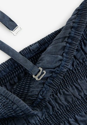 Navyblauer Stoff mit geraffter Textur, ausgestattet mit verstellbaren Trägern und metallischen Beschlägen zum Verschließen. Mit elastischen Nähten verziert.
