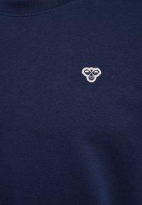 Navyblåt stof med et lille hvidt broderet biemblem nær det øvre midterområde.