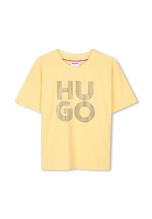 Gul bomull T-skjorte med korte ermer og rund hals. Har store "HUGO"-bokstaver i et prikket mønster over forsiden.