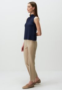 Top senza maniche di colore blu navy con finitura testurizzata, abbinato a pantaloni attillati beige chiaro con cuciture laterali e scarpe slip-on beige.