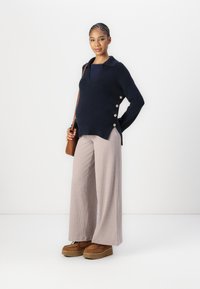 Navy knit sweater with a collar and side button details, paired with light ribbed wide-leg pants and brown platform shoes.