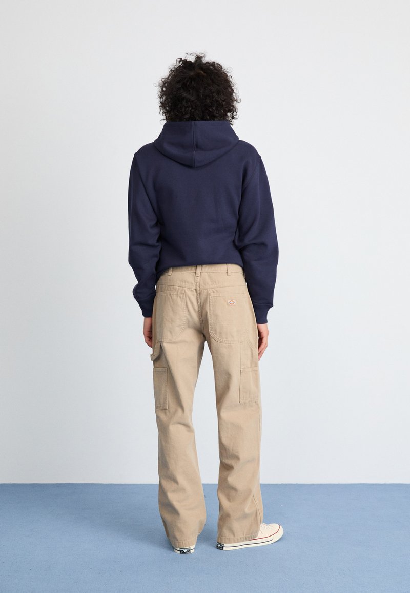 Felpa navy con tasca a marsupio abbinata a pantaloni cargo beige con ampie tasche laterali e un logo discreto sulla tasca posteriore.