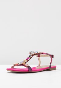Ploché růžové sandály s popruhy s hadím vzorem zdobené vícebarevnými drahokamy a bočním zapínáním na přezku.
