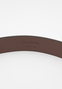 Brun læderbælte med en glat tekstur, prydet med præget "PULL&BEAR" branding og størrelse 85 indeni.