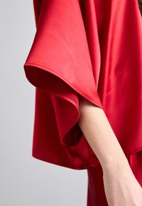 Gros plan d’une personne portant un vêtement rouge, ample, avec de larges manches fluides couvrant partiellement son bras.