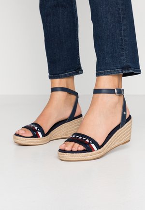 Hakken sandalen met een marineblauwe stoffen bovenkant, enkelbandje en jute-gevlochten zool. Kenmerkt rode en witte geborduurde strepen op de voorkant.