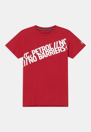 Camiseta roja de manga corta con cuello redondo y texto diagonal blanco en negrita que dice "PETROL NO BARRIERS" en el frente.