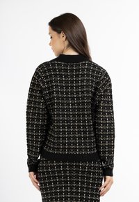 Maglione lavorato a maglia nero e oro con un motivo a quadri testurizzato, polsini e bordo a coste, con colletto tondo e vestibilità leggermente ampia.