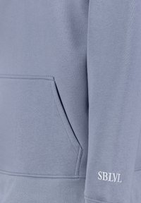 Light blue sweatshirt featuring a kangaroo pocket and ribbed hem. The left sleeve displays the text "SBLVL" in white. Soft texture, casual design.