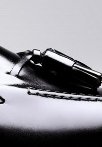 Black leather shoe featuring a sleek design, smooth texture, decorative tassels, and contrasting stitching along the upper edge.