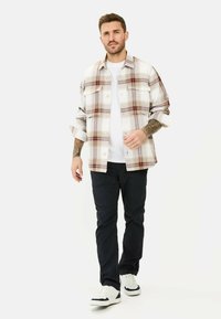 Beige, rote und marinefarbene karierte Hemd mit langen Ärmeln und Brusttaschen. Kombiniert mit schwarzen Hosen und weißen Turnschuhen.