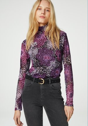 Langsleeve coltrui in paarse bloemenprint, gemaakt van een gladde stof, gecombineerd met hoge zwarte jeans en een zwarte riem.
