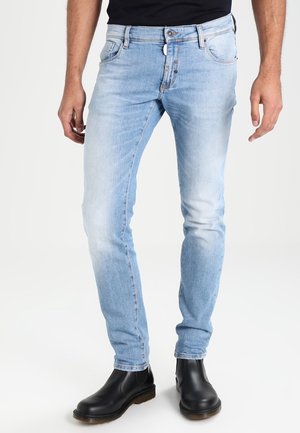Hellblaue Slim-Fit-Jeans mit einem verwaschenen Finish, Fünf-Taschen-Design und Knopfverschluss, kombiniert mit schwarzen Stiefeletten.