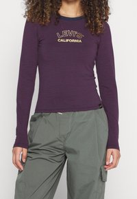 Lilangärbige Langarmshirt mit navy horizontalen Streifen, bedruckt mit dem Text "LEVI'S CALIFORNIA" in Gold, kombiniert mit grünen Cargo-Hosen.