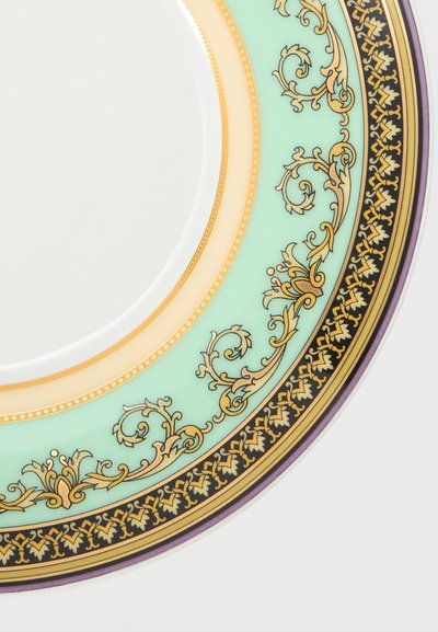 Λευκό πορσελάνινο πιάτο με περίτεχνα μοτίβα σε χρυσό, μαύρο και ανοιχτό πράσινο γύρω από την άκρη, σε λευκό φόντο.