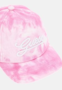 Gorra de tela en tonos rosa con diseño de tie-dye que presenta el logotipo blanco "Guess" bordado en la parte frontal, con una visera curva y un botón en la parte superior.