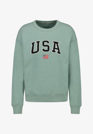 Jasnozielona bluza z okrągłym dekoltem z dużymi czarnymi literami "USA" i małą flagą amerykańską poniżej napisu.
