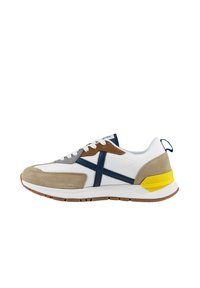 Zapatilla blanca con acentos en gris, marrón y azul marino. Hecha de ante y malla, presenta una franja lateral prominente y un detalle en el talón en color amarillo.