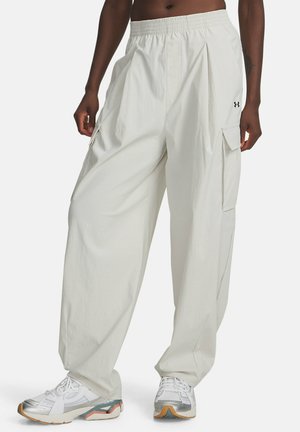 Persoon in losse witte cargobroek met elastische taille en witte sneakers, staand voor een effen achtergrond.
