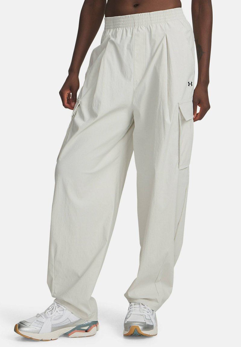 Persona con pantalones cargo blancos holgados y cintura elástica, y zapatillas blancas, de pie contra un fondo sencillo.