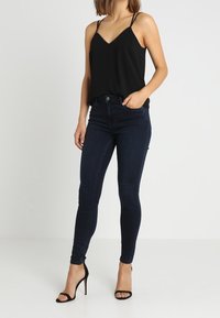 Svart ärmlös topp med tunna band, parat med mörkblå skinny jeans och svarta stiletto-klackar, med en figurnära silhuett.